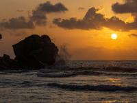 Wellen gischten beim Sonnenuntergang gegen den Felsblock an der Anse Severe - La Digue